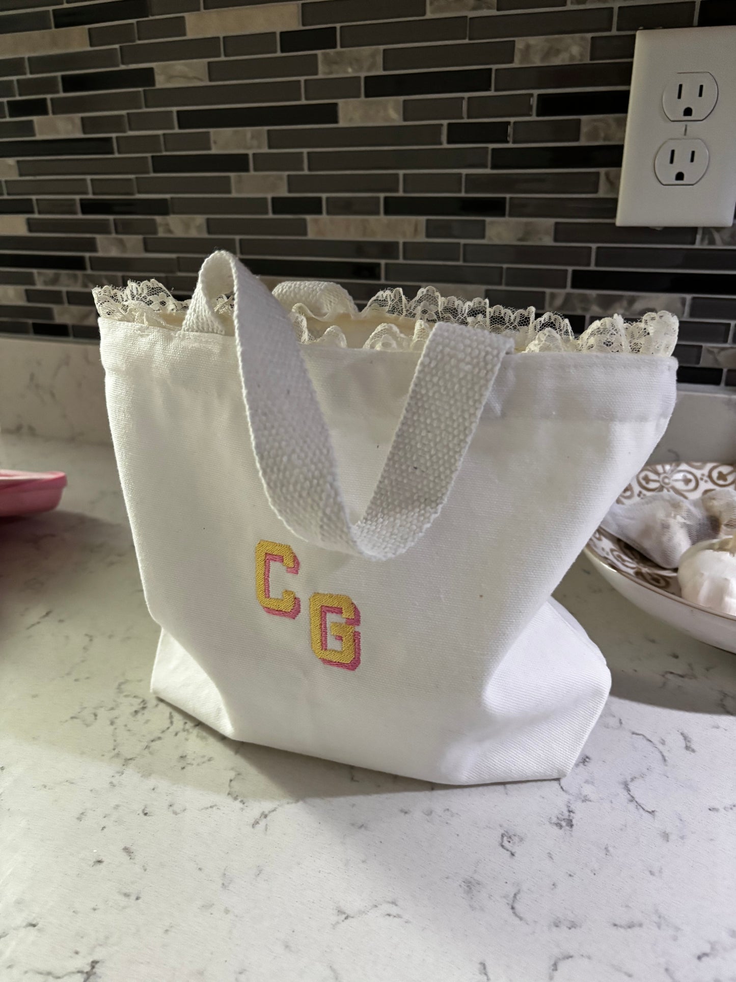 White lace-trimmed fabric with 'CG' initials on a tiled wall.
