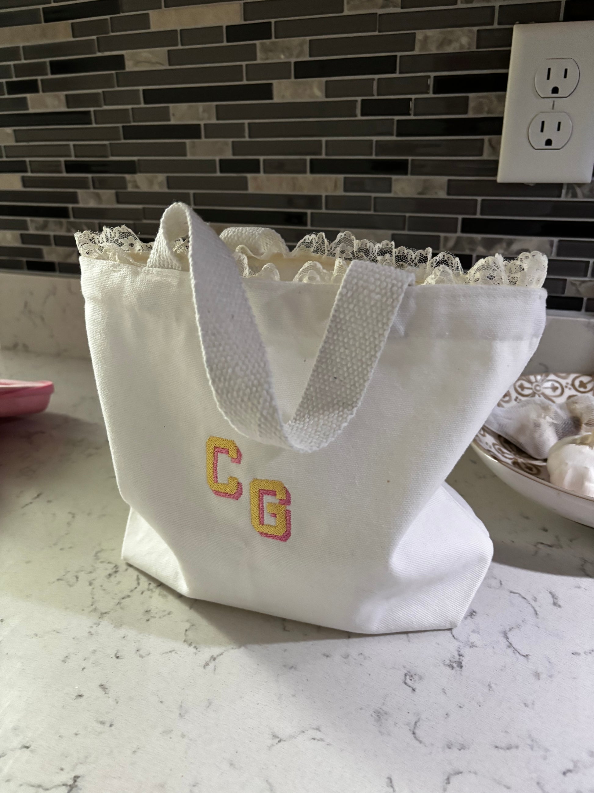 White lace-trimmed fabric with 'CG' initials on a tiled wall.
